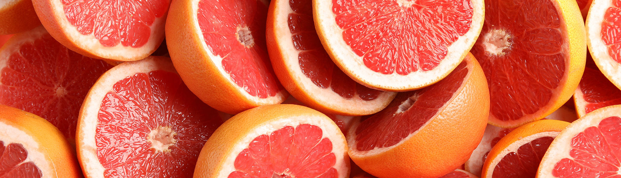 Mehrere Pampelmusenhälften sind in einer Nahaufnahme zu sehen, die ihr rosarotes, saftiges Inneres und ihre gelb-orangefarbene Schale zeigt. Die Früchte überlappen sich und füllen den gesamten Rahmen aus.