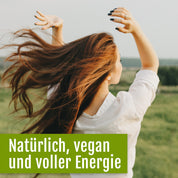 Eine fröhliche Frau mit langen braunen Haaren und einem weißen Hemd streckt auf einer grünen Wiese die Arme in die Höhe. Deutscher Bildtext: Natürlich, vegan und voller Energie – dank Naturland-Bio-Chlorella-Tabletten von gse.organic.supplements und wertvollem Vitamin B12.