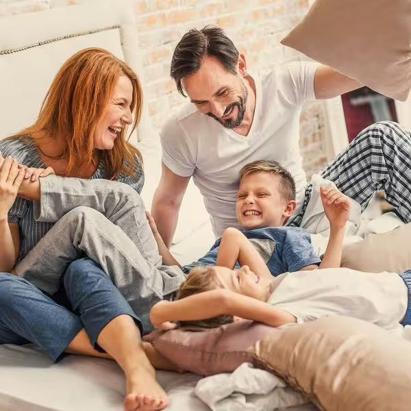 Eine fröhliche vierköpfige Familie, zwei Erwachsene und zwei Kinder, liefert sich eine lebhafte Kissenschlacht auf einem gemütlichen Bett, ihre Energie so lebendig wie CitroPlus® 1200 forte (Bio) von gse.organic.supplements.